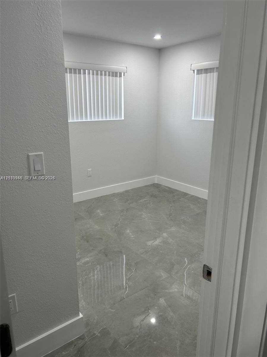 Interior space featuring large-format grey stone-finish tile flooring, neutral walls, two windows with vertical blinds, and recessed lighting