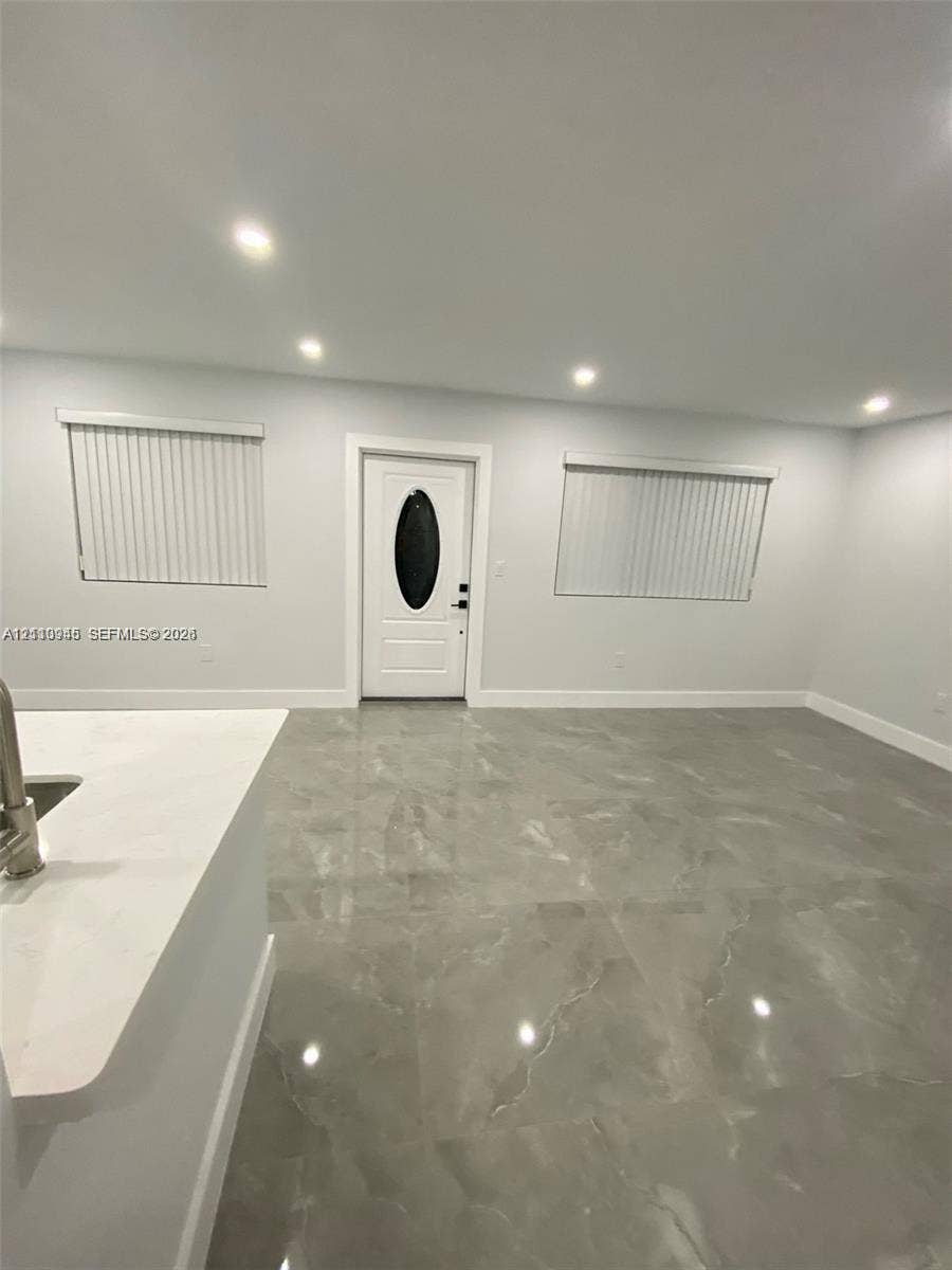 Large-format tile flooring, recessed ceiling lighting, and a white front entry door with an oval glass inset, complemented by neutral walls and window treatments