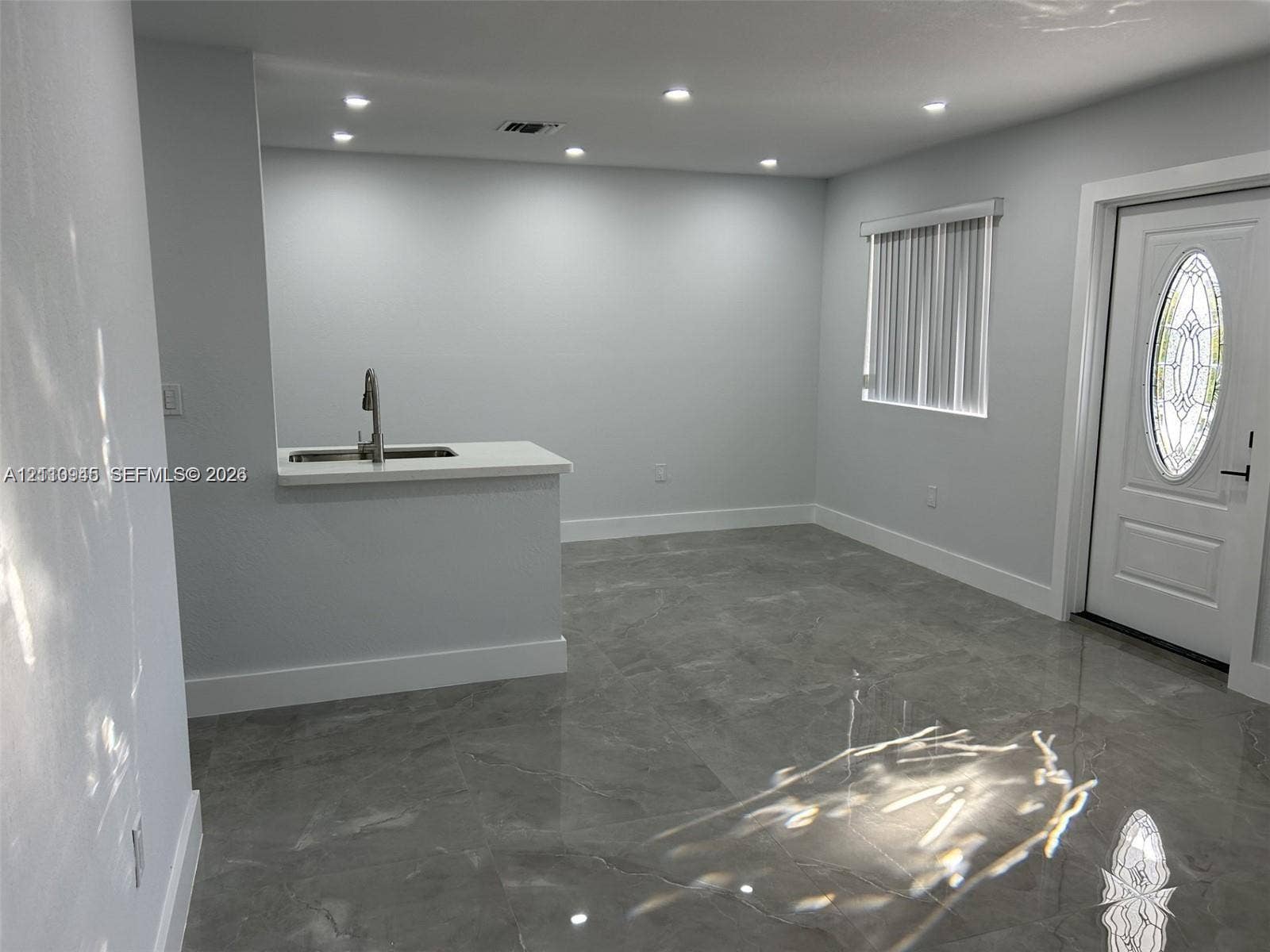 Large-format stone-finish tile flooring, recessed ceiling lighting, pass-through counter with a stainless steel sink, and an exterior door with an oval decorative glass insert