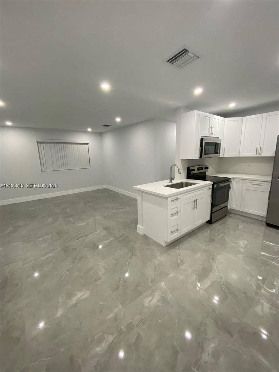Kitchen area featuring white shaker-style cabinetry, a central island with an undermount sink, recessed lighting, and large-format porcelain tile flooring