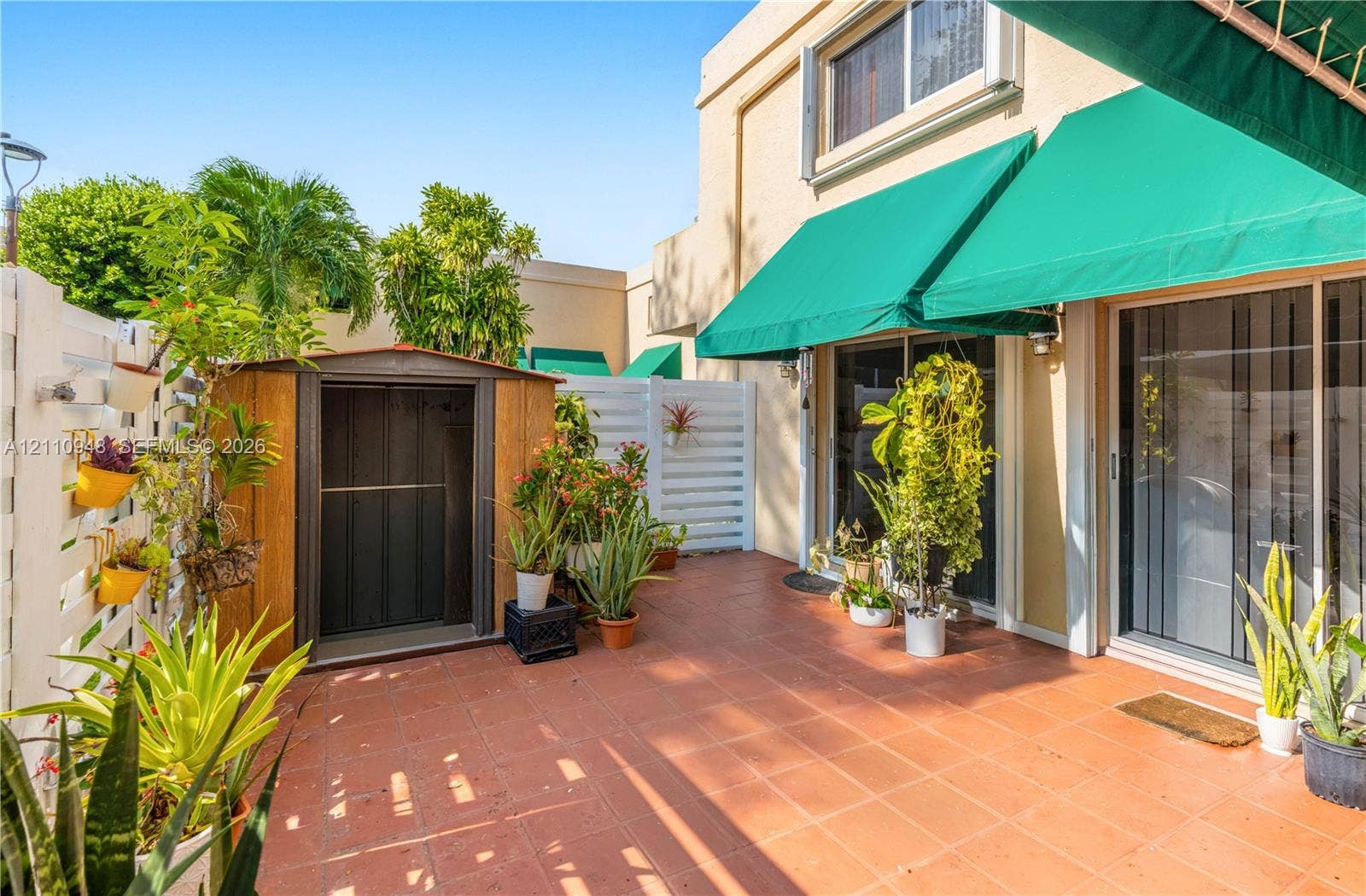Enclosed patio featuring terracotta tile flooring, green retractable fabric awnings, and white privacy fencing