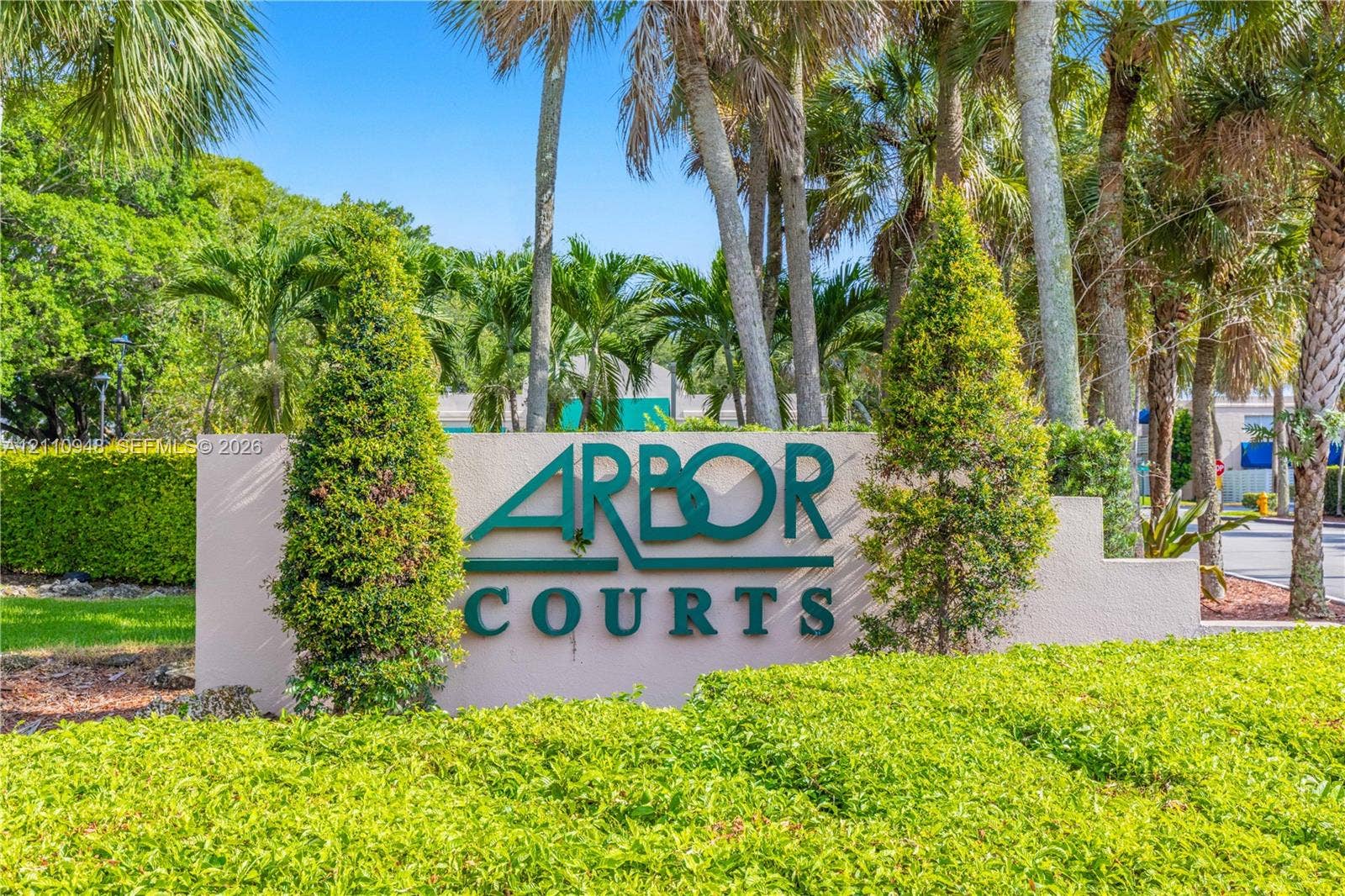 Stucco monument signage featuring dimensional lettering, landscaped hedge borders, and mature palm trees