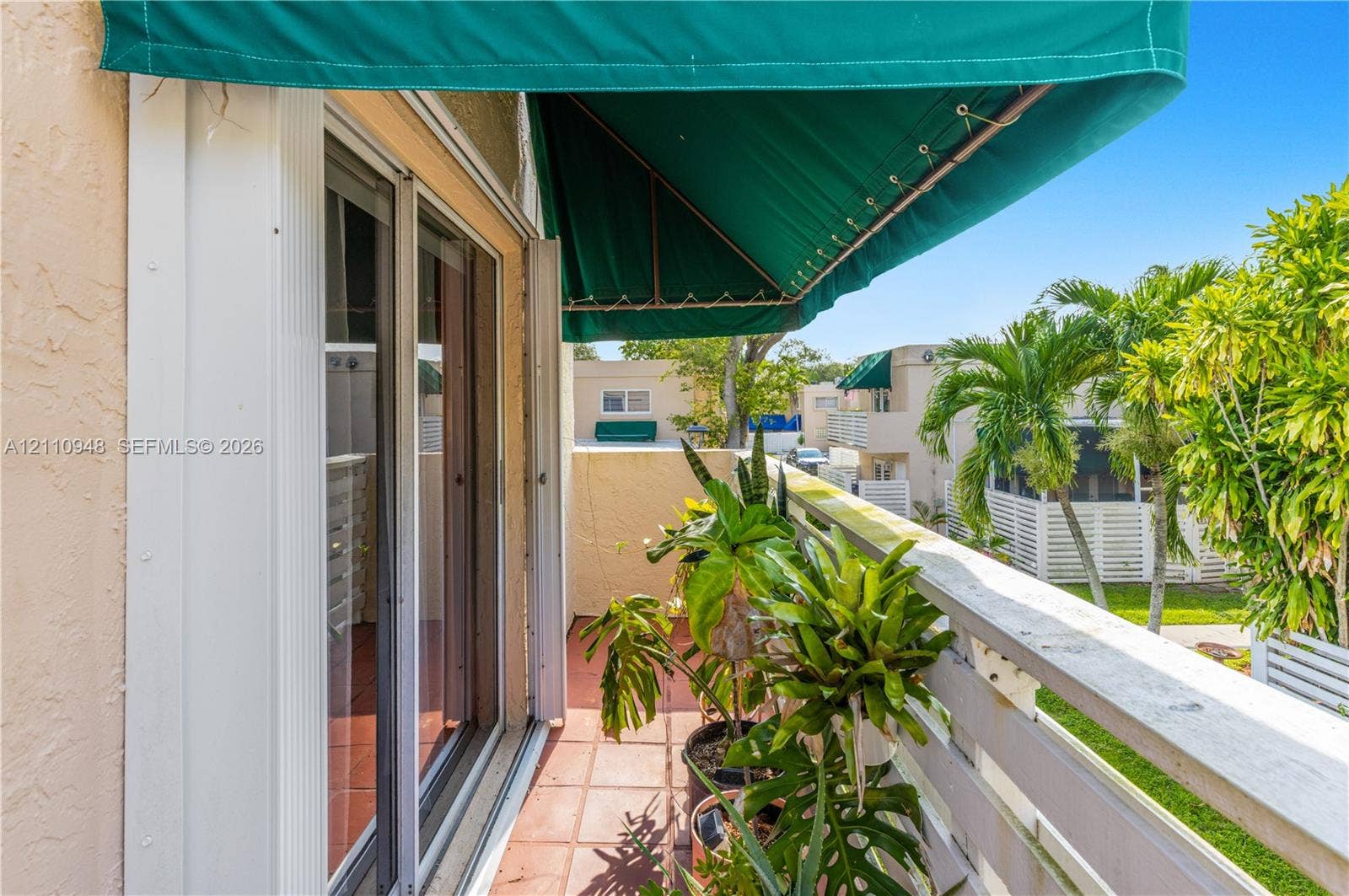 Private balcony featuring a fixed green fabric awning, tiled flooring, and a white wooden railing