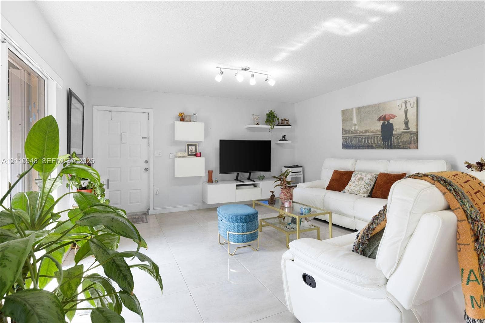 Open-concept living space featuring large-format tile flooring, wall-mounted white cabinetry, floating shelving, and multi-bulb track lighting