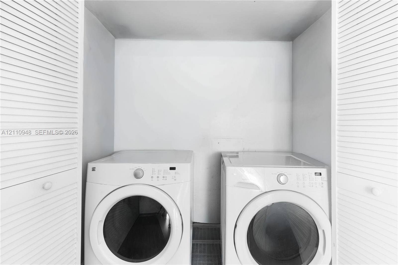 Laundry area featuring white front-load appliances and dual louvered-style closet doors