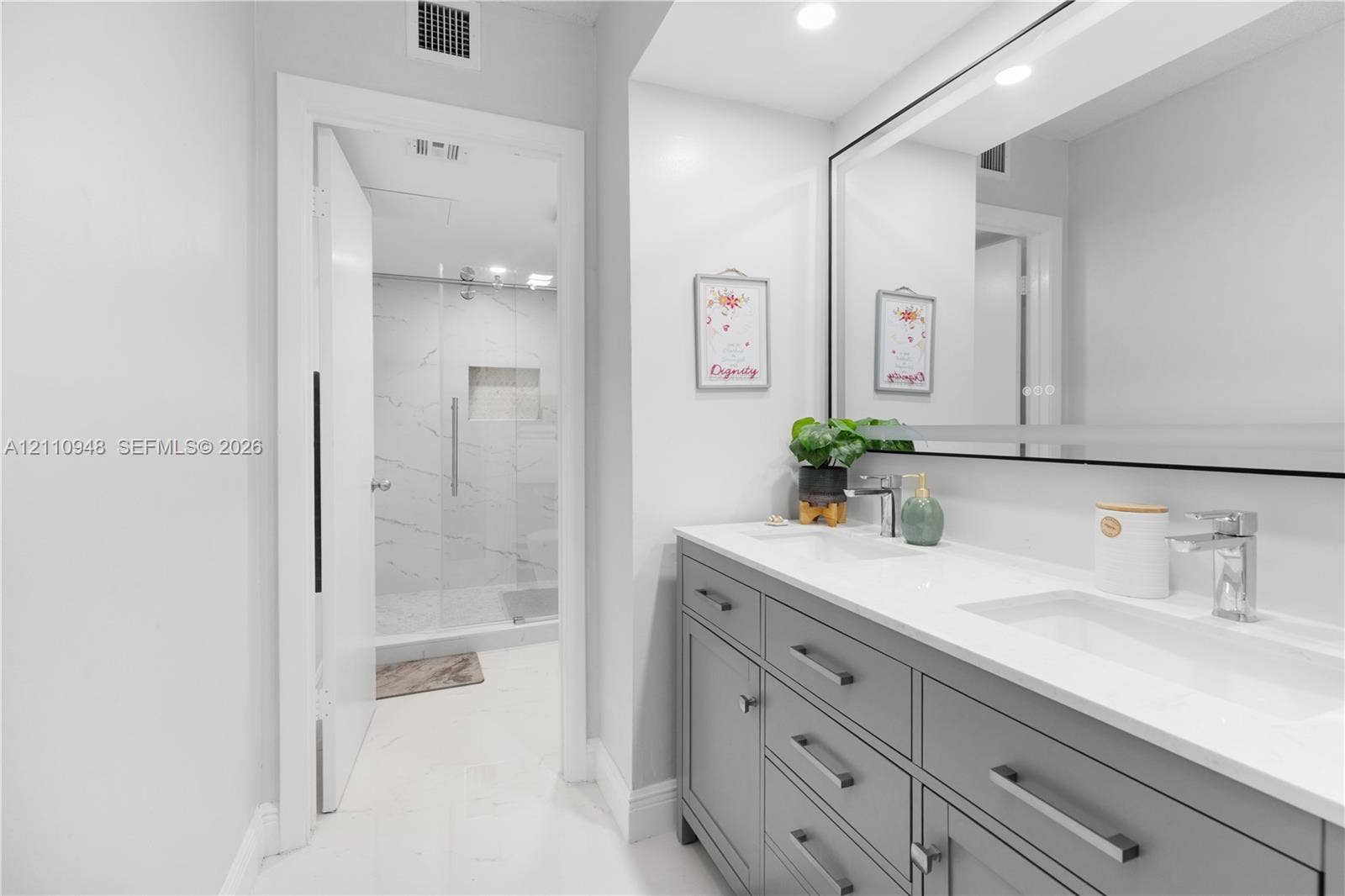 Dual-sink vanity with grey cabinetry, white solid-surface countertops, and a wide integrated mirror