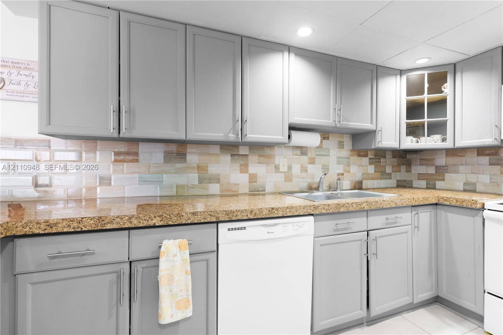 Kitchen featuring gray shaker-style cabinetry, multi-tonal subway tile backsplash, stone-surface countertops, and an undermount double-basin sink