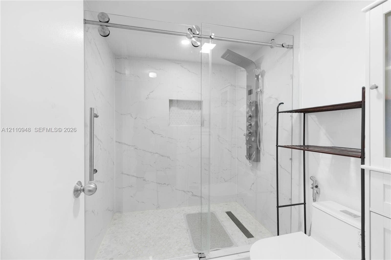 Walk-in shower featuring a sliding glass door, floor-to-ceiling stone-patterned wall tile, recessed niche, and integrated rainfall shower panel with body sprayers