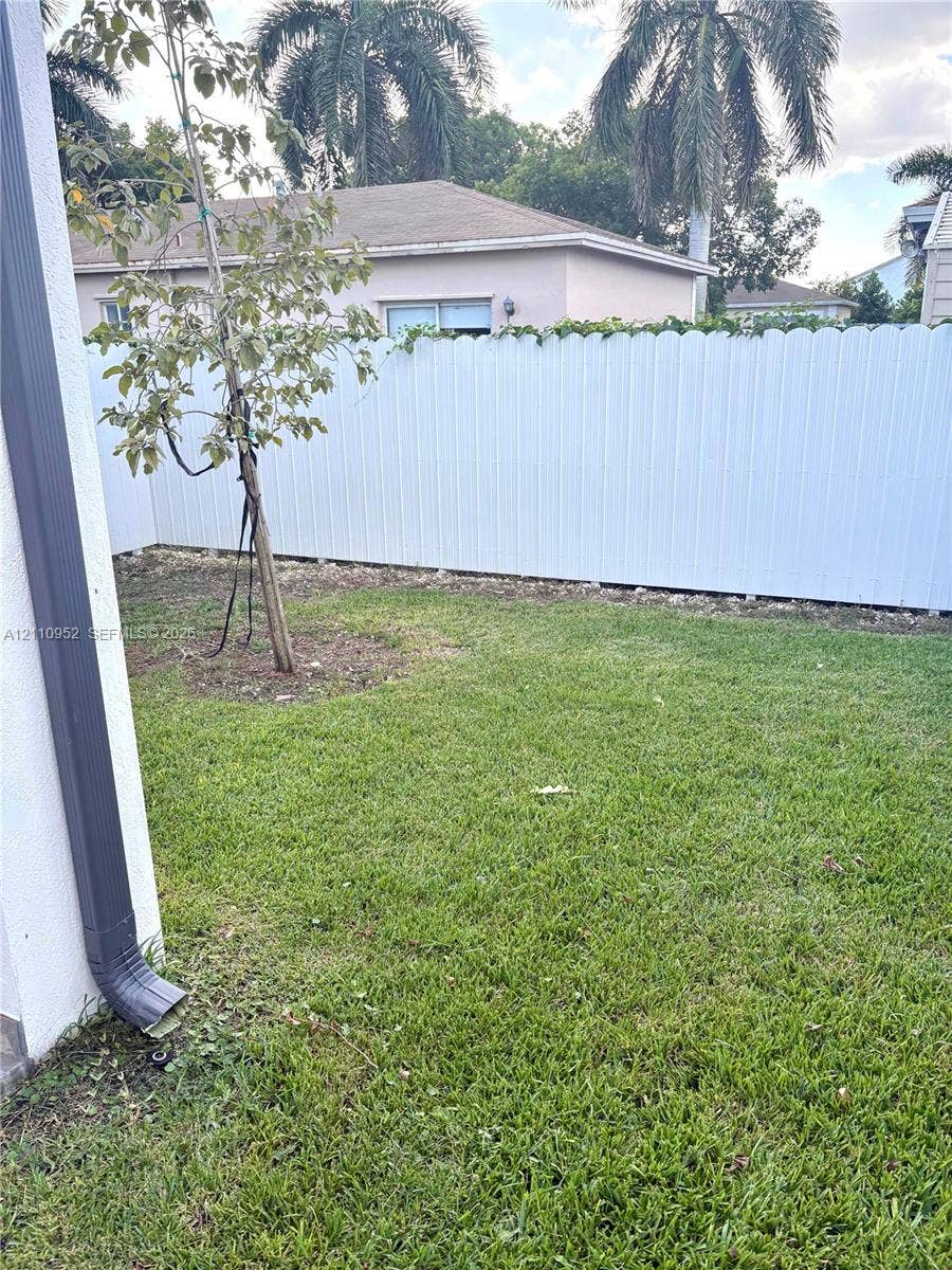 1225 NW 9 Avenue, #0, Florida City, Florida City, FL 33034 Backyard featuring a white scalloped-top privacy fence, manicured lawn, and mature foliage