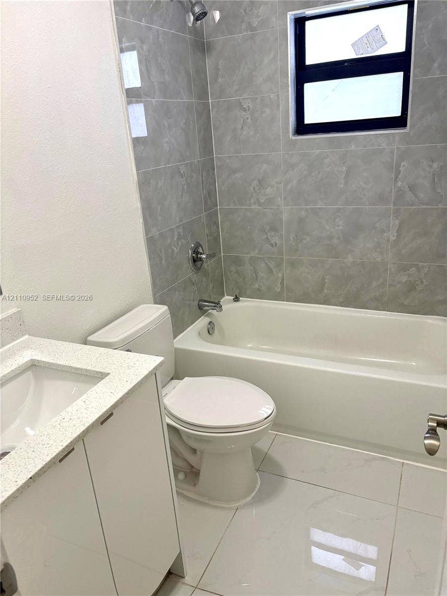 1225 NW 9 Avenue, #0, Florida City, Florida City, FL 33034 Bathroom featuring large-format gray wall tiling, a white composite tub with metallic fixtures, polished white floor tiling, and a vanity topped with a speckled white composite counter