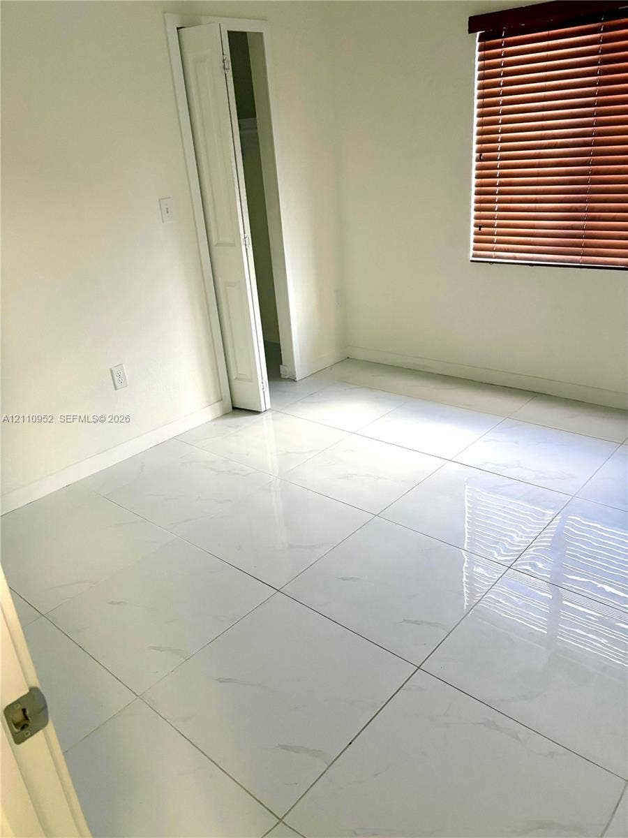 1225 NW 9 Avenue, #0, Florida City, Florida City, FL 33034 Large-format tile flooring with a light marbled finish, accompanied by a bi-fold closet door and horizontal slat window blinds