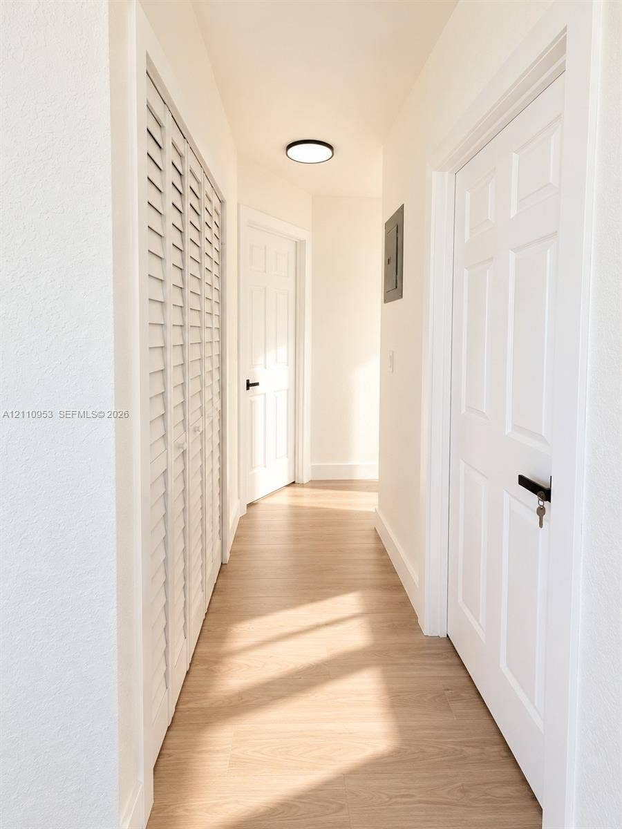 Hallway featuring wood-finish flooring, white six-panel doors with matte black hardware, white louvered closet doors, and a flush-mount circular ceiling fixture
