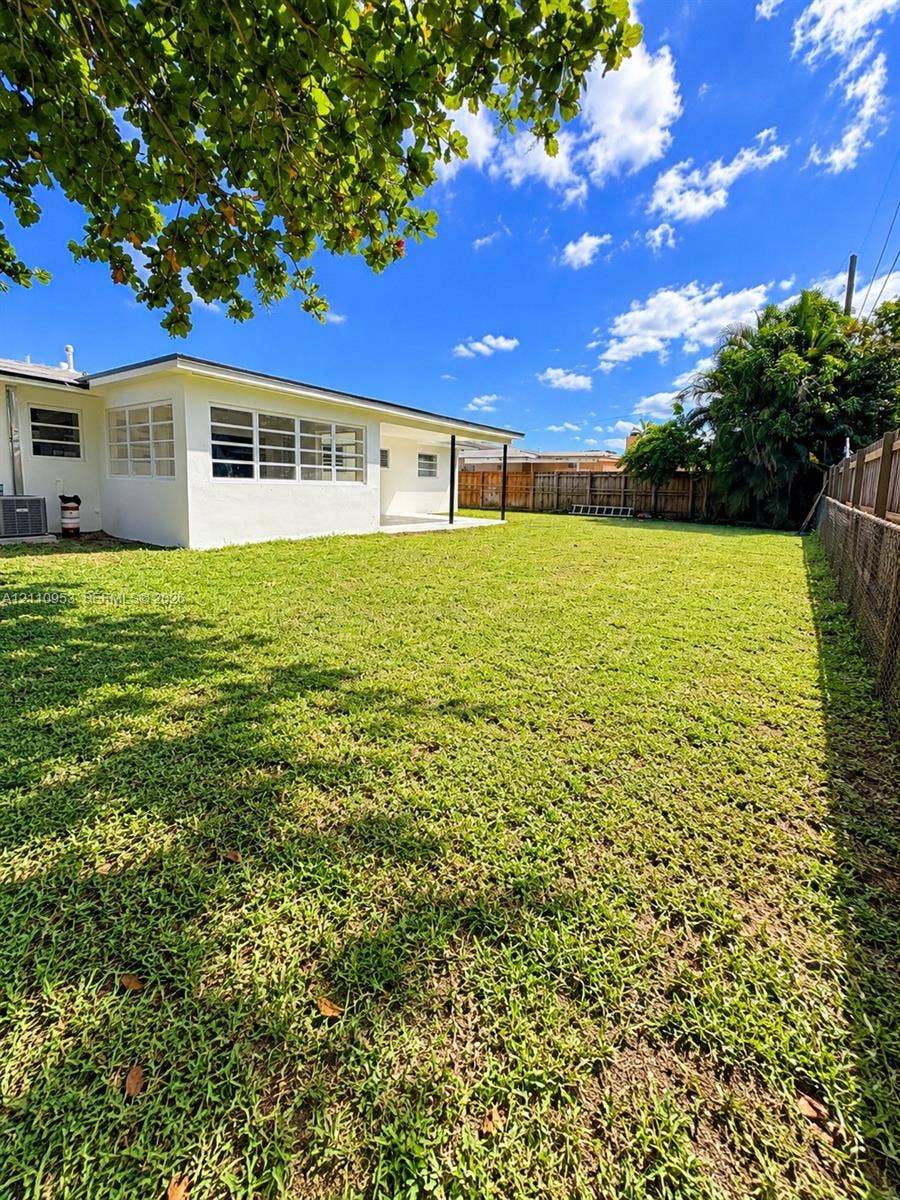 Expansive backyard featuring a large grass lawn, perimeter wood fencing, masonry boundary wall, and a covered patio area