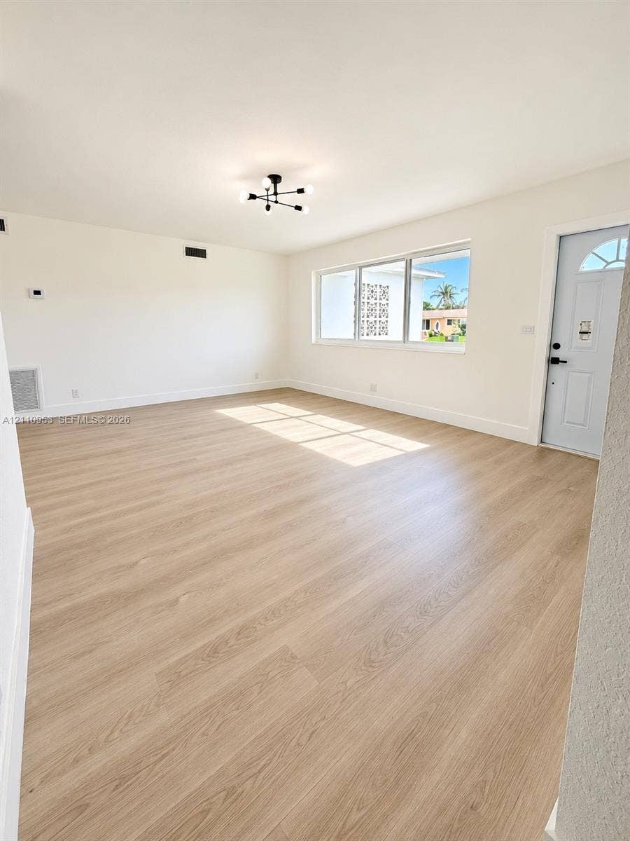 Interior space featuring wood-finish flooring, a modern sputnik-style ceiling light fixture, large windows, and a panelled exterior door with decorative glass inlay
