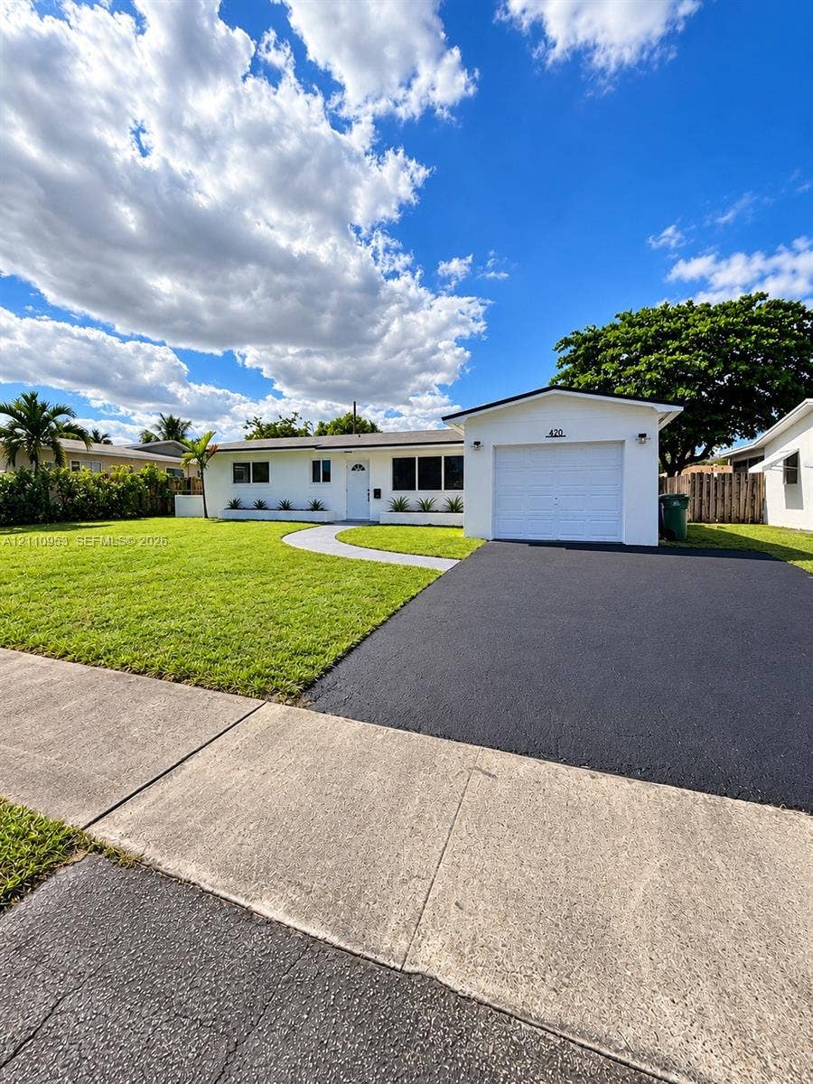 Single-story exterior featuring a white facade, attached one-car garage, asphalt driveway, curved concrete walkway, and manicured lawn