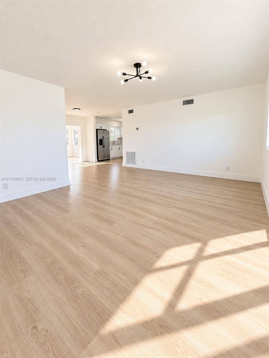 Open-concept interior featuring wood-finish flooring, a contemporary six-arm matte black chandelier, and neutral wall tones