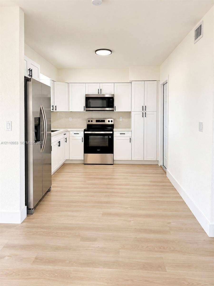 Kitchen featuring white shaker-style cabinetry, wood-finish flooring, and a suite of stainless steel appliances including a built-in microwave and range