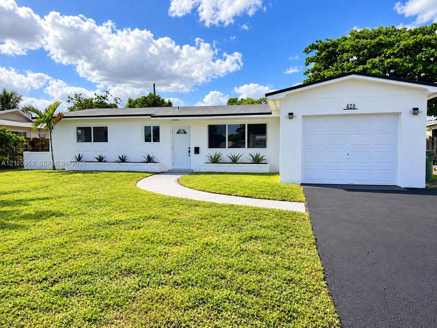 Single-story exterior featuring a crisp white finish, integrated concrete planter beds, a paved walkway, and an attached garage with an asphalt driveway
