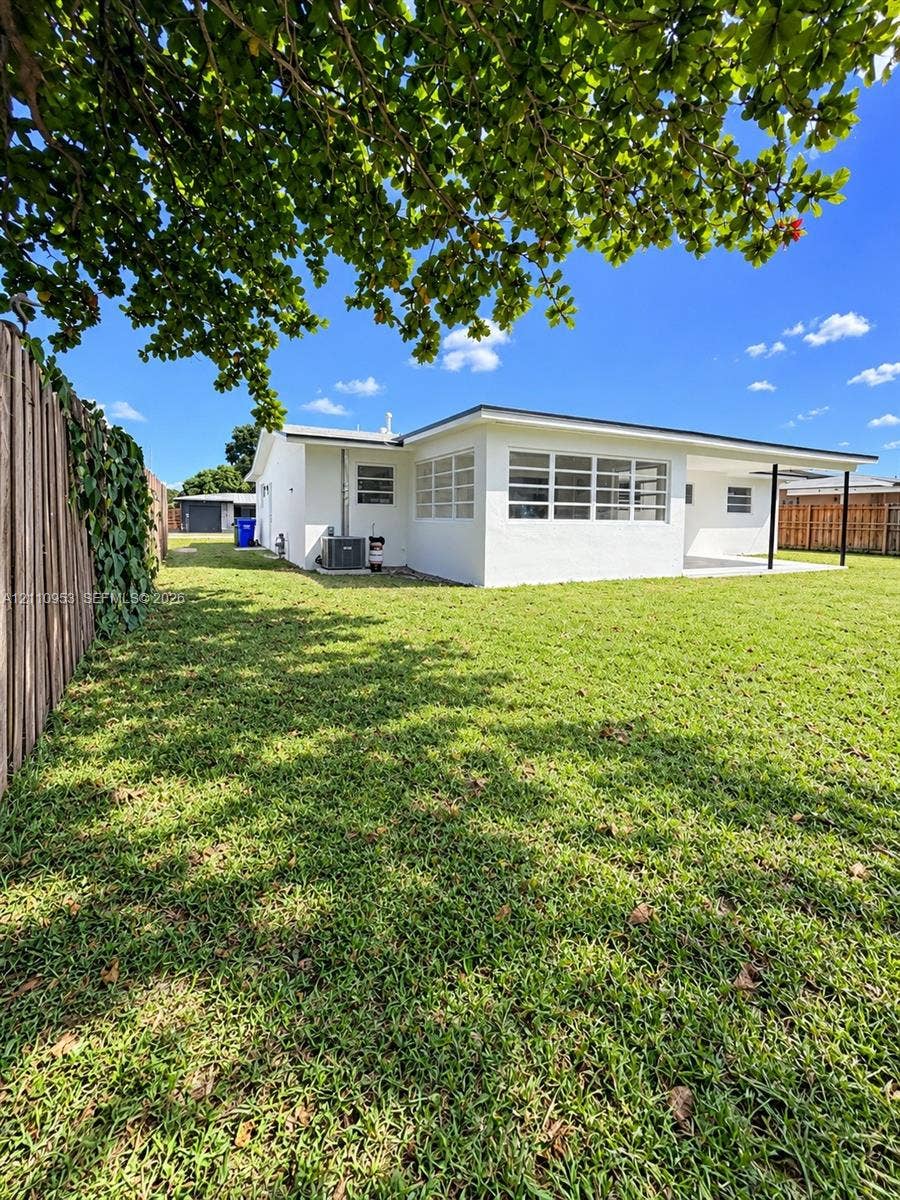 Expansive backyard featuring a manicured lawn, wood fencing, covered patio, and multi-pane windows