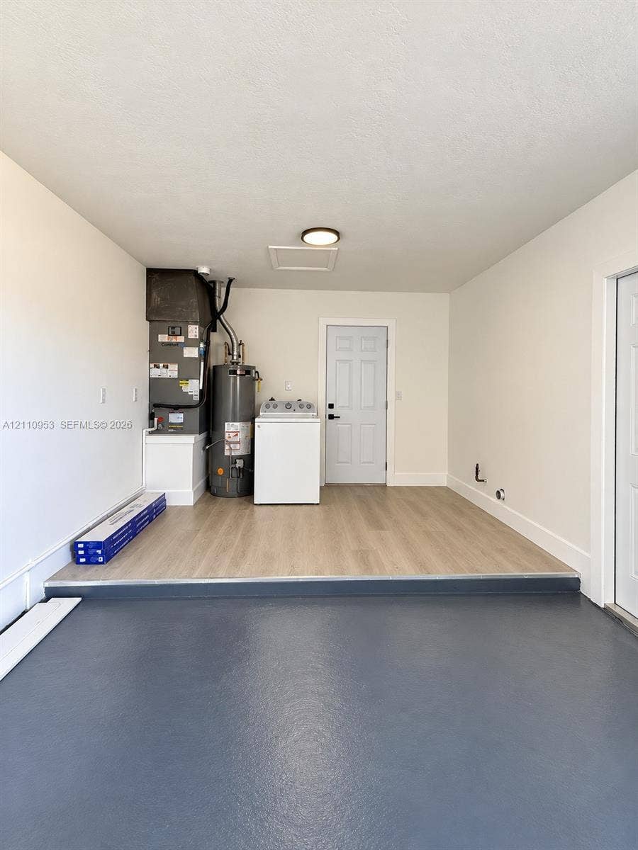 Dedicated utility area featuring wood-finish flooring, a six-panel door, painted walls, and a mounted ceiling light fixture