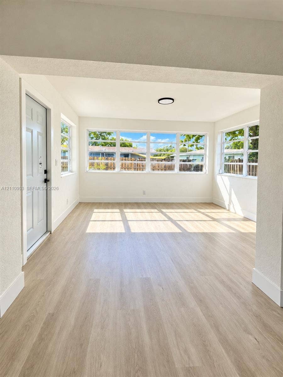 Neutral color palette with wood-finish flooring, multiple windows providing natural illumination, and a flush-mount circular ceiling fixture