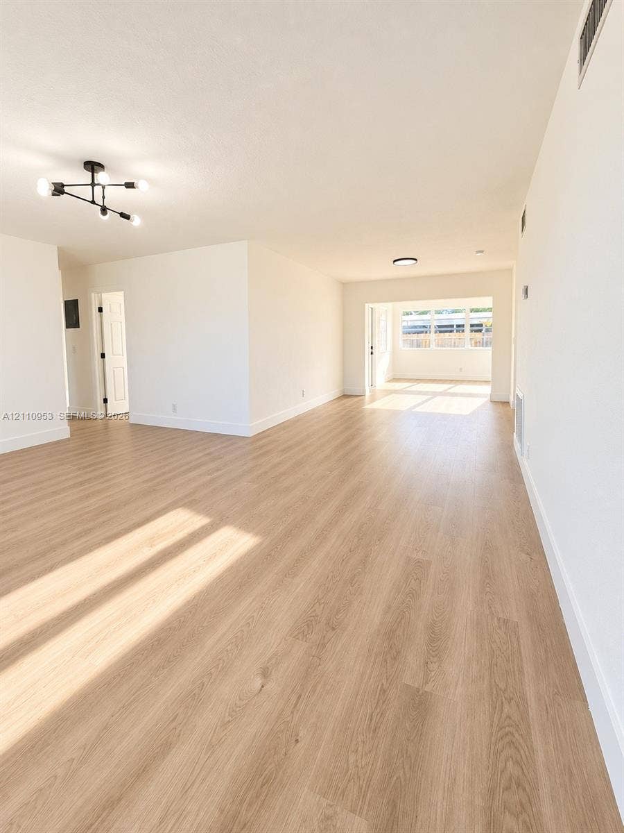 Open interior space featuring wood-finish flooring, neutral walls, and a multi-arm geometric ceiling fixture