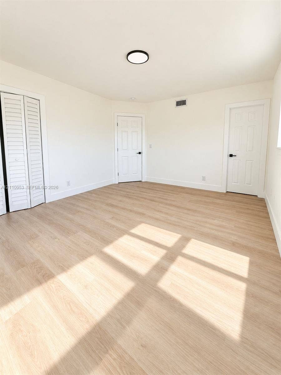 Interior room featuring wood-finish flooring, white walls, louvered closet doors, six-panel interior doors with matte black hardware, and a flush-mount circular ceiling light