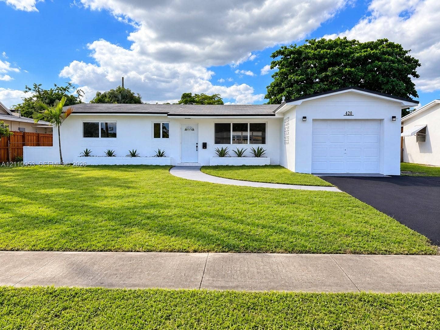 Single-story residence with white stucco exterior, integrated one-car garage, manicured front lawn, built-in concrete planters, and paved driveway