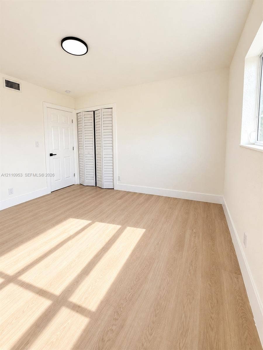 Interior room featuring wood-finish flooring, white louvered bi-fold closet doors, a six-panel door with matte black hardware, and a circular LED flush-mount light fixture