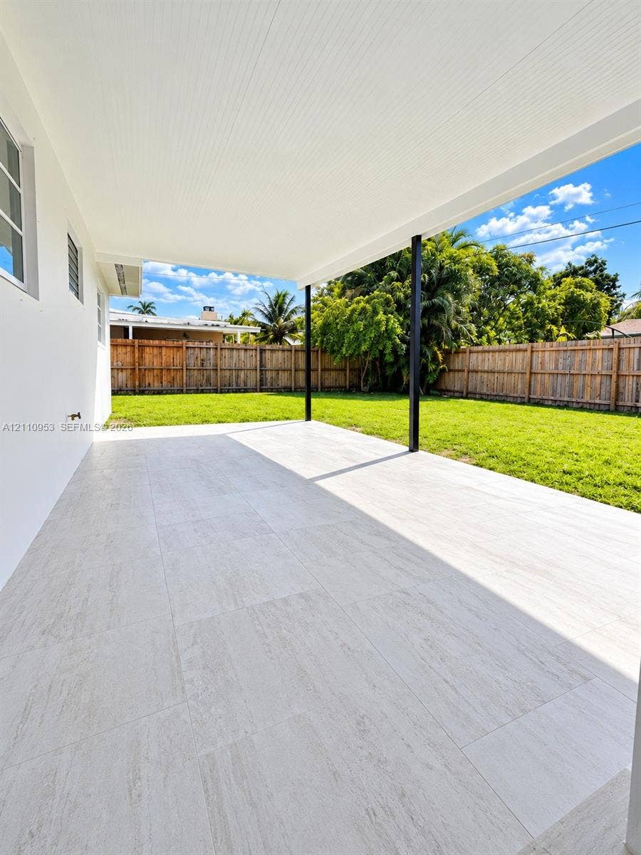 Covered patio featuring large-format stone-style tile flooring, a flat ceiling, thin-profile black support columns, and a fenced backyard with grass lawn