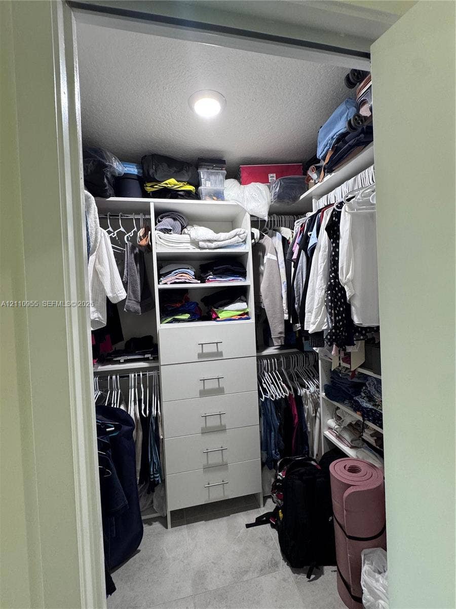 4636 NW 84th Avenue, #35, Doral, FL 33166 Walk-in closet featuring white built-in shelving, a five-drawer storage unit with metal pulls, dual-level hanging rods, and stone-finish flooring
