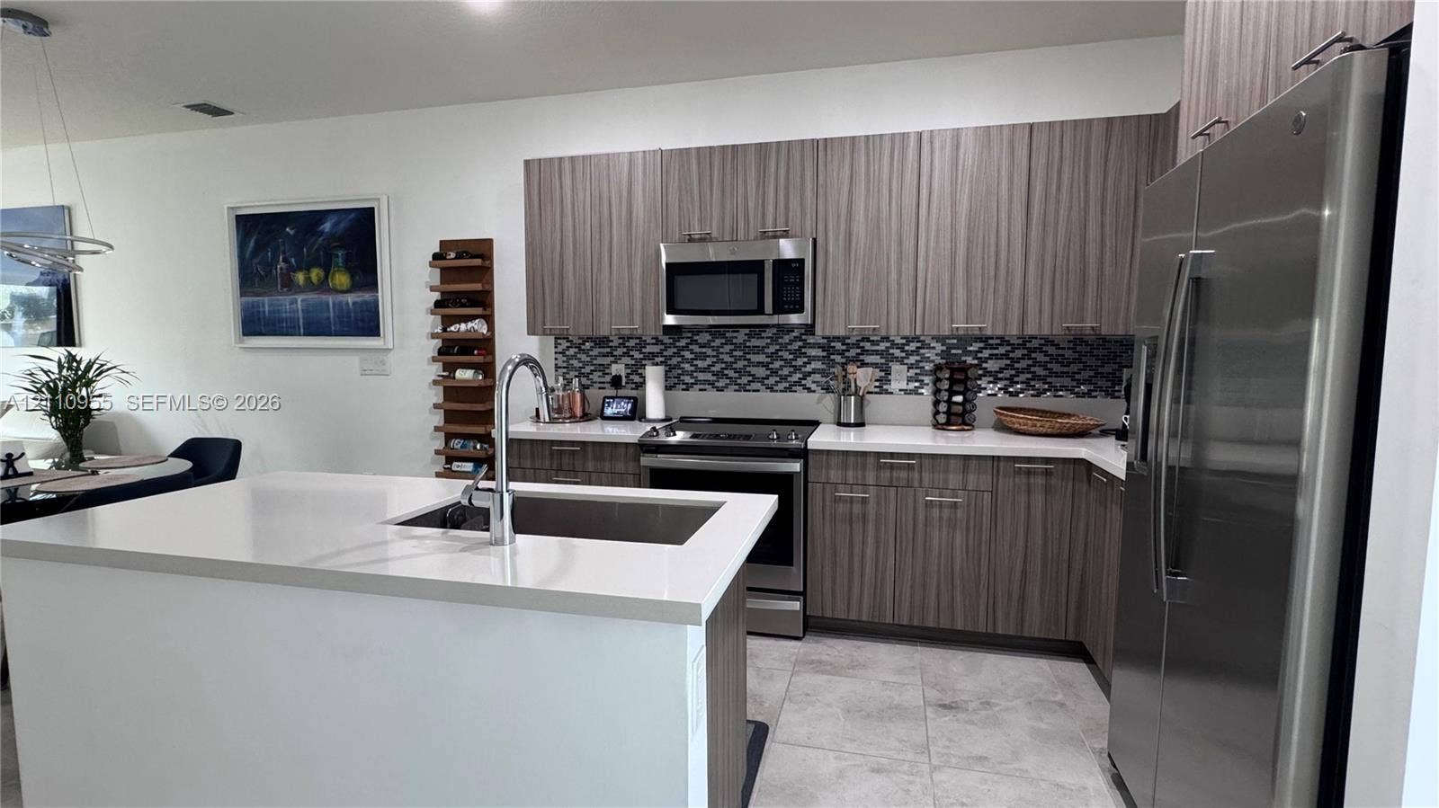 4636 NW 84th Avenue, #35, Doral, FL 33166 Kitchen featuring wood-finish cabinetry, quartz countertops, a patterned tile backsplash, stainless steel appliances, and a center island with a stainless steel undermount sink