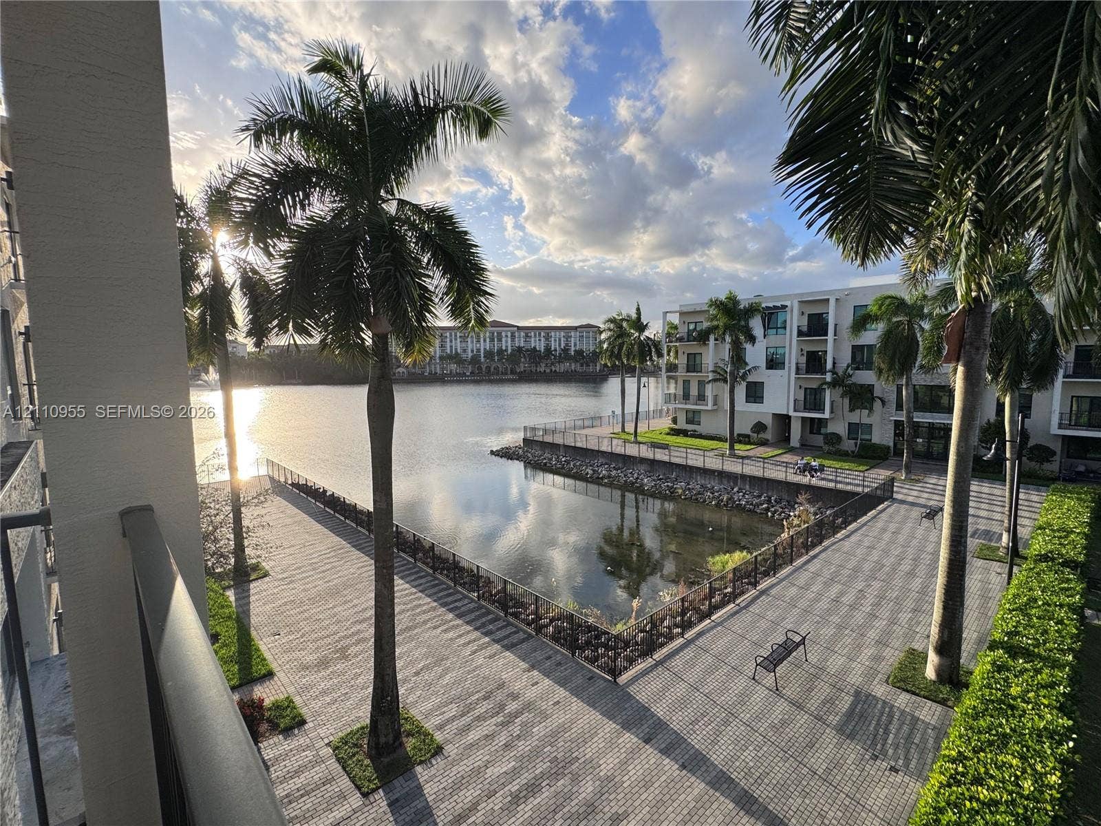 4636 NW 84th Avenue, #35, Doral, FL 33166 Waterfront terrace featuring paved walkways, integrated metal railings, mature palm trees, and bulkhead stone detailing