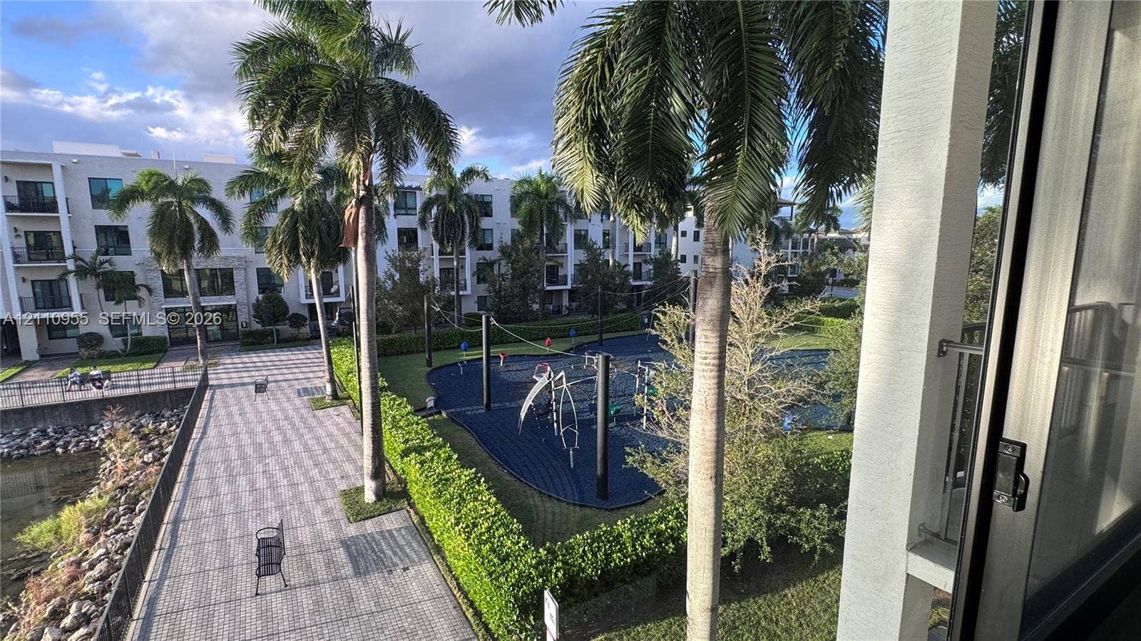 4636 NW 84th Avenue, #35, Doral, FL 33166 Exterior space featuring a paved walkway, mature palm trees, manicured hedges, and a recreation area with a rubberized surface