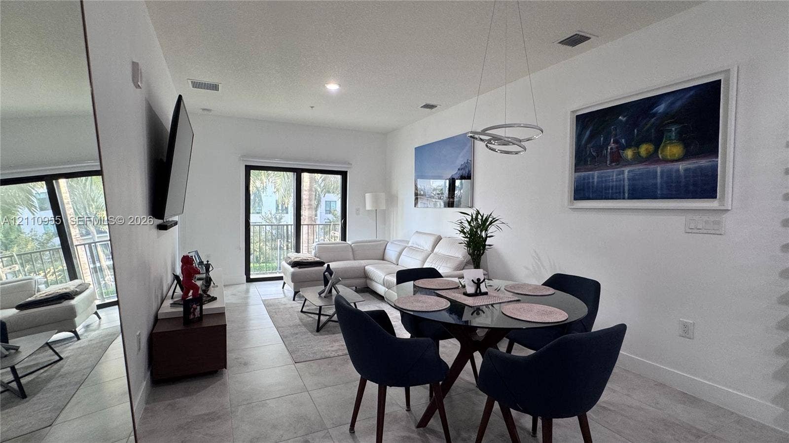 4636 NW 84th Avenue, #35, Doral, FL 33166 Open-concept interior featuring large-format tile flooring, a contemporary circular multi-ring pendant light, full-height wall mirror, and sliding glass doors leading to an exterior balcony