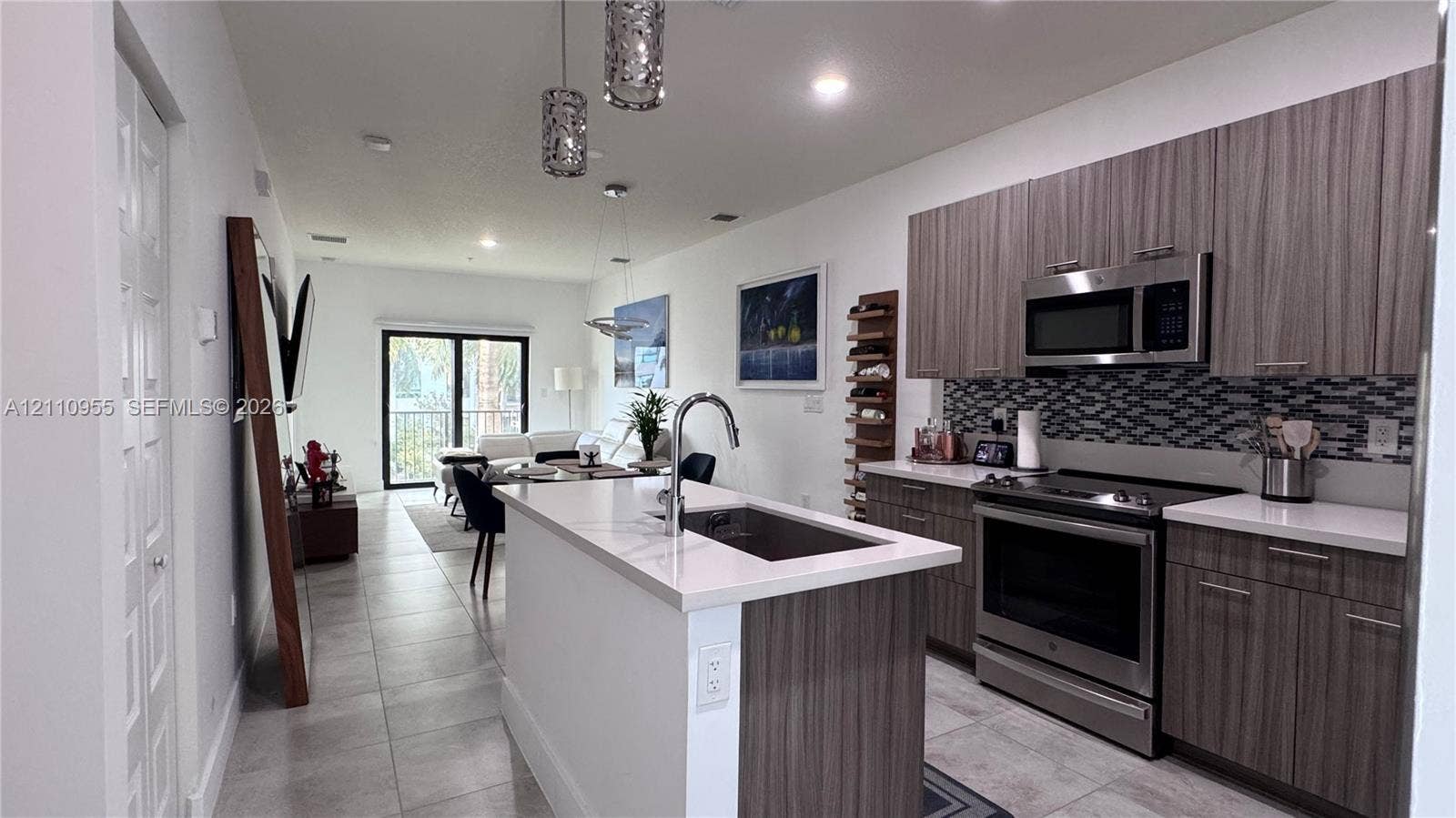 4636 NW 84th Avenue, #35, Doral, FL 33166 Kitchen featuring flat-panel wood-finish cabinetry, light-toned stone countertops, a multi-tonal mosaic tile backsplash, stainless steel appliances, and a central island with an integrated sink and gooseneck faucet