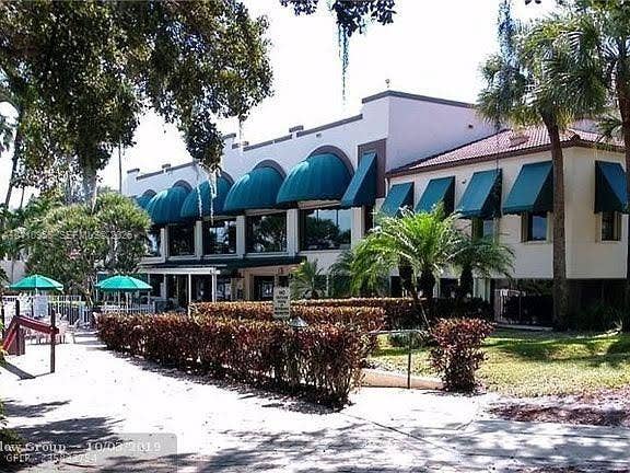 2120 SW 94th Terrace, #404, Davie, FL 33324 Two-story stucco exterior featuring arched windows, decorative green fabric awnings, a tile roof, and landscaped hedging