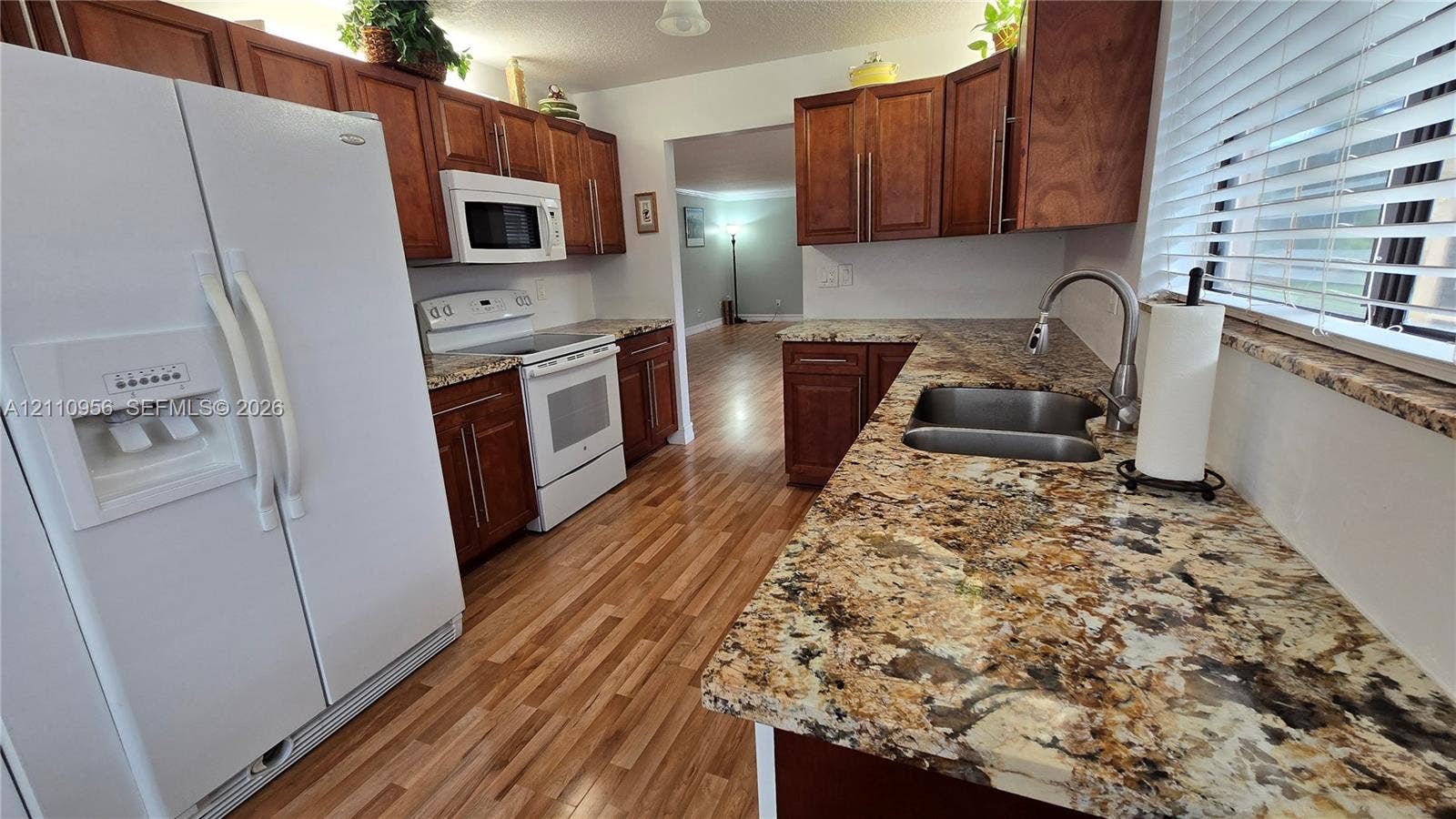2120 SW 94th Terrace, #404, Davie, FL 33324 Kitchen featuring stained wood cabinetry, stone countertops, double-basin stainless steel sink with pull-down faucet, white appliance package, and wood-finish flooring