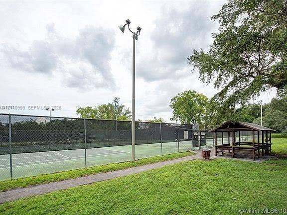 2120 SW 94th Terrace, #404, Davie, FL 33324 Tennis court featuring chain-link perimeter fencing, pole-mounted high-intensity lighting, and a wooden gazebo