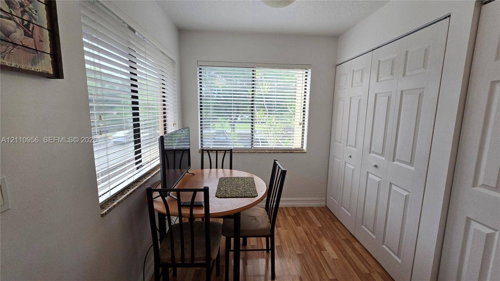 2120 SW 94th Terrace, #404, Davie, FL 33324 Neutral-toned interior room featuring wood-finish flooring, dual windows with horizontal blinds, and a large closet with paneled double-fold doors