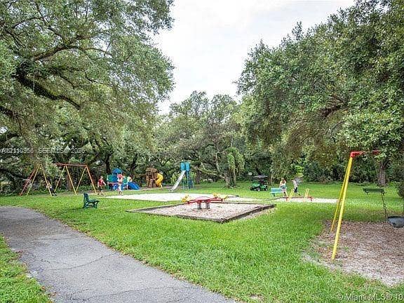 2120 SW 94th Terrace, #404, Davie, FL 33324 Outdoor recreational area featuring multiple swing sets, a slide, climbing structures, sand-filled play surfaces, and mature canopy trees