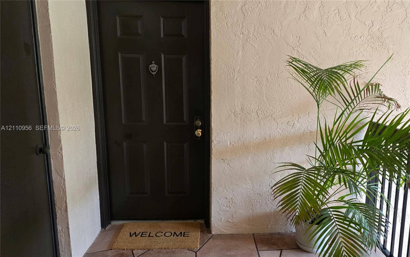2120 SW 94th Terrace, #404, Davie, FL 33324 Dark-finished four-panel entry door featuring a metallic door knocker and hardware, set against a textured stucco exterior wall with tile flooring
