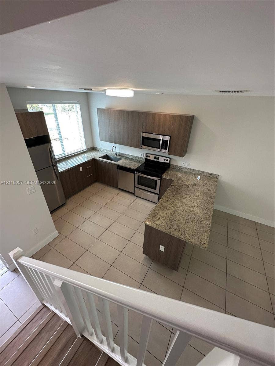 12115 NE 5th Avenue, #12115, North Miami, North Miami, FL 33161 Kitchen featuring flat-panel wood-finish cabinetry, stone-surface countertops, stainless steel appliances, ceramic tile flooring, and a peninsula with counter seating