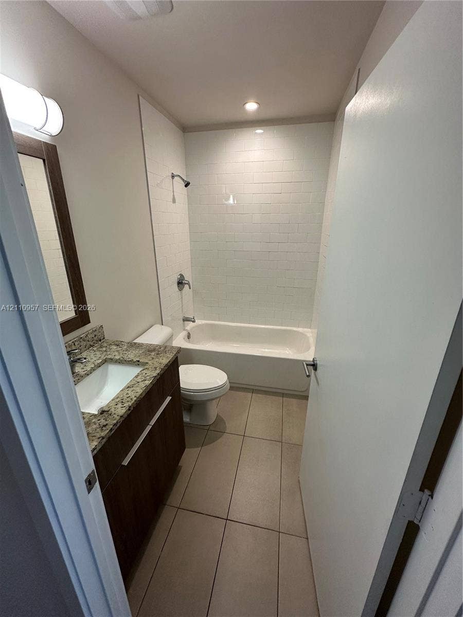 12115 NE 5th Avenue, #12115, North Miami, North Miami, FL 33161 Bathroom featuring a wood-finish vanity with a stone countertop, an integrated sink, floor-to-ceiling white subway tile shower surround, and neutral floor tile