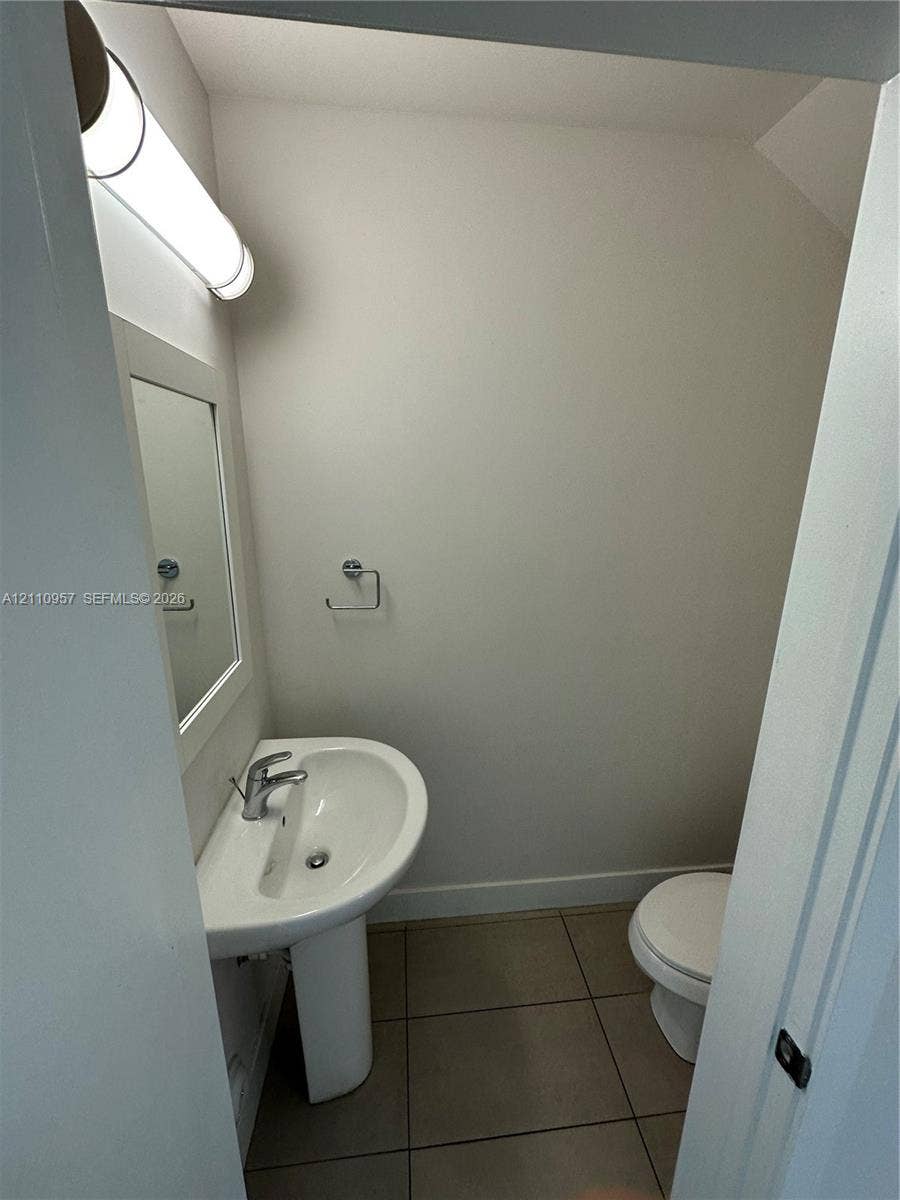 12115 NE 5th Avenue, #12115, North Miami, North Miami, FL 33161 Powder room featuring a pedestal sink, wall-mounted light fixture, framed mirror, and tile flooring