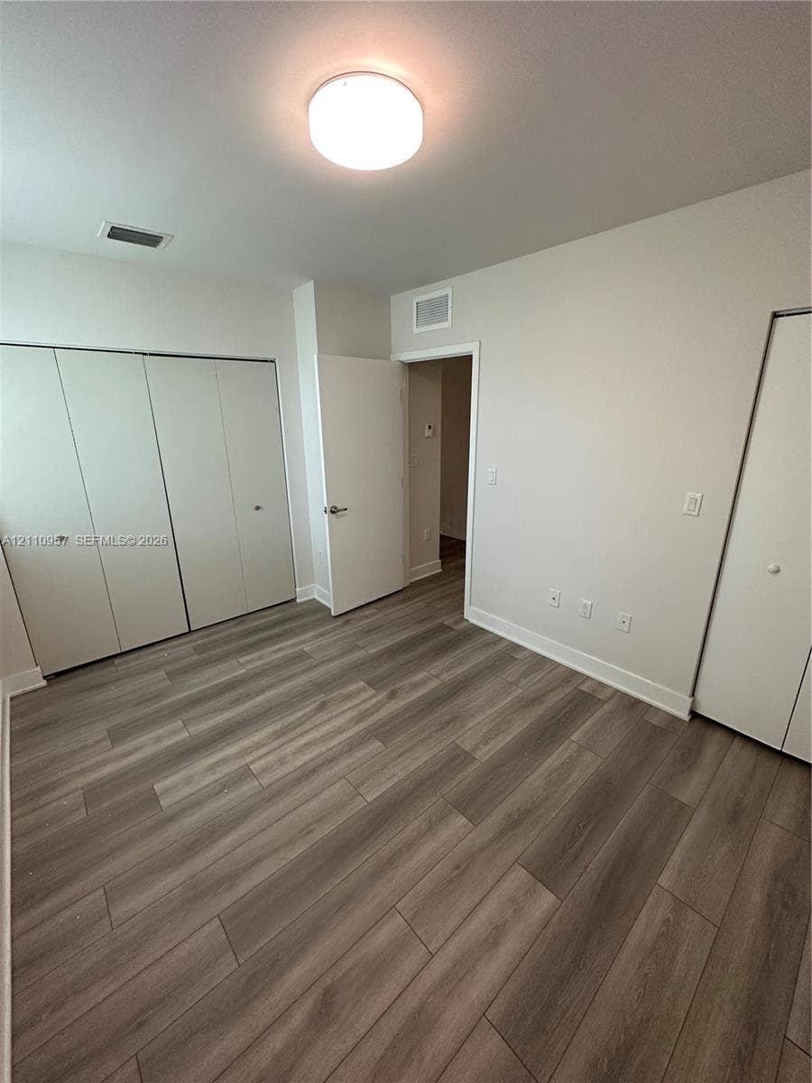 12115 NE 5th Avenue, #12115, North Miami, North Miami, FL 33161 Room featuring wood-finish flooring, dual bi-fold door closets, neutral wall paint, and a flush-mount overhead light fixture
