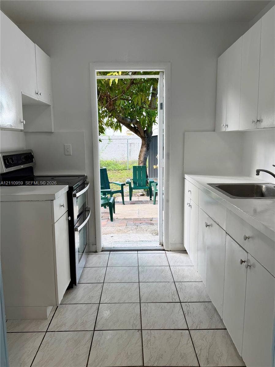 Kitchen featuring white cabinetry, solid-surface countertops, tile flooring, and integrated black range