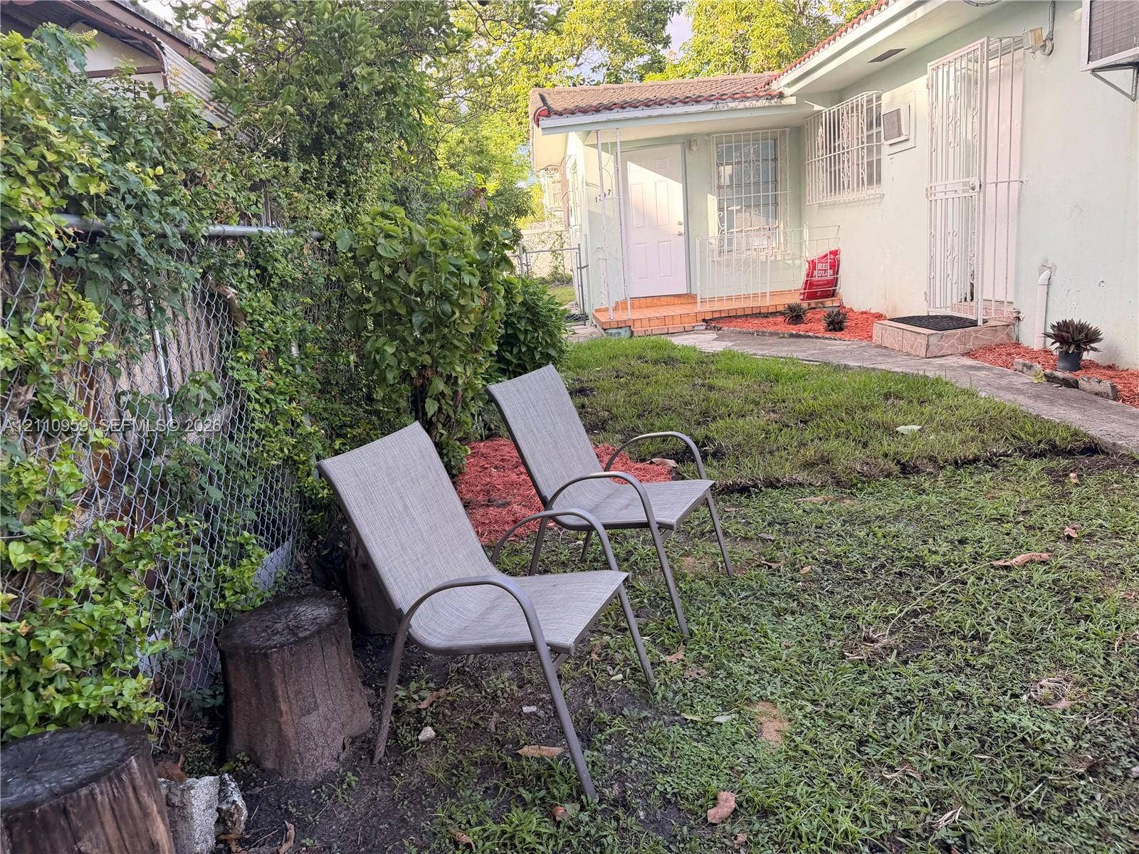 Exterior side yard featuring a concrete walkway, mulch ground cover, and chain-link fencing