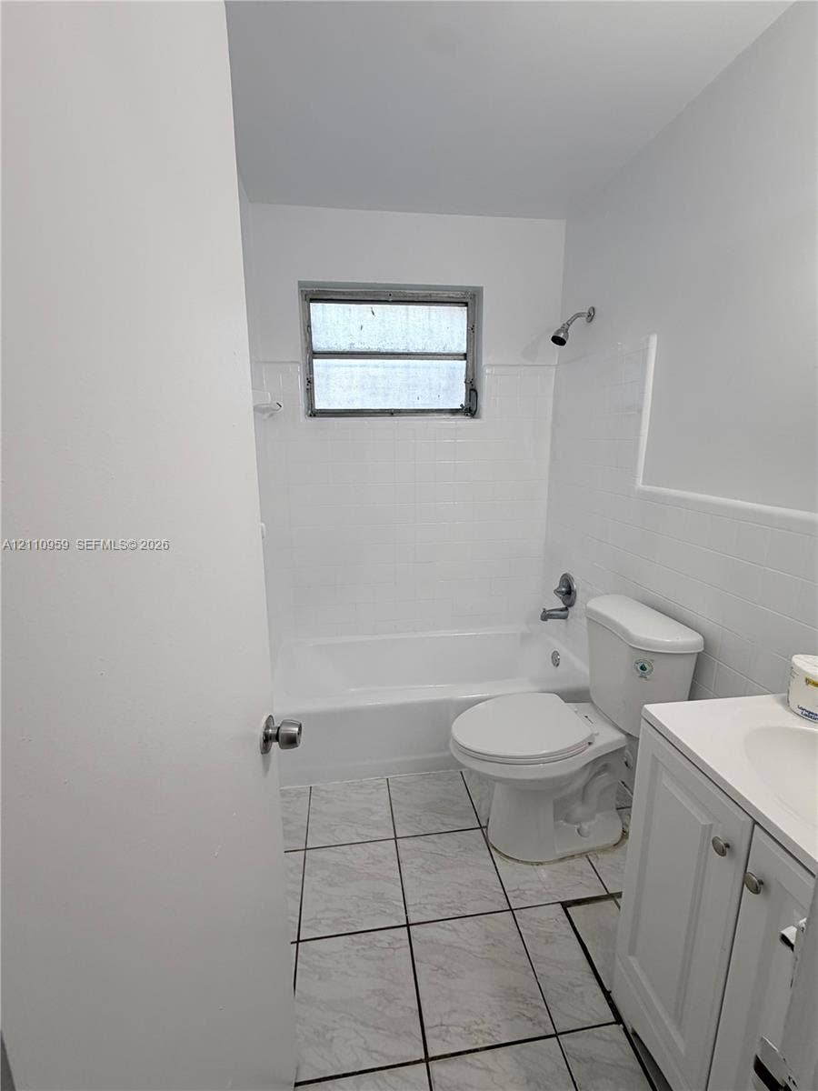 Bathroom featuring white ceramic wall tile, tub-shower combination, vanity with integrated basin, and neutral-toned tile flooring