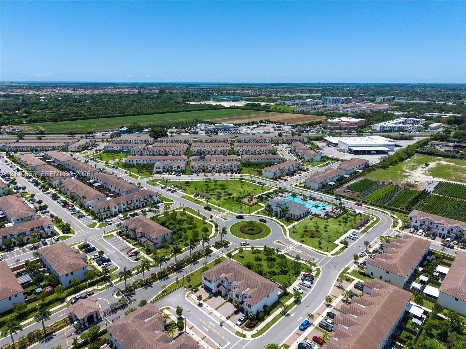 23436 SW 129th Avenue, #23436, Homestead, Homestead, FL 33032 Aerial perspective of a multi-unit residential community featuring paved roads, a central traffic circle, manicured green spaces, and a swimming pool facility